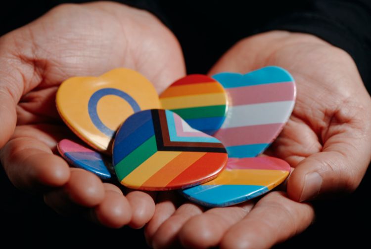 Hands open holding buttons of different flags. Pride Flag Button, Trans Flag, Intersex Flag.